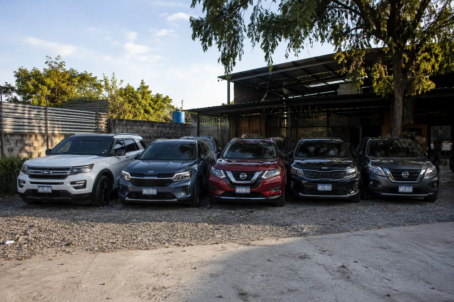 Cinco vehículos de propietarios estacionados en fila bajo un techo al atardecer